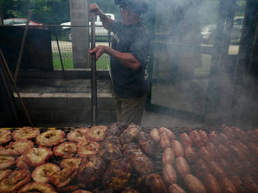 A chef prepares a traditional Argentine asado, showing the open-fire grilling of meat