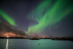 Green aurora borealis dancing over a still lake at night, Keflavik, Iceland