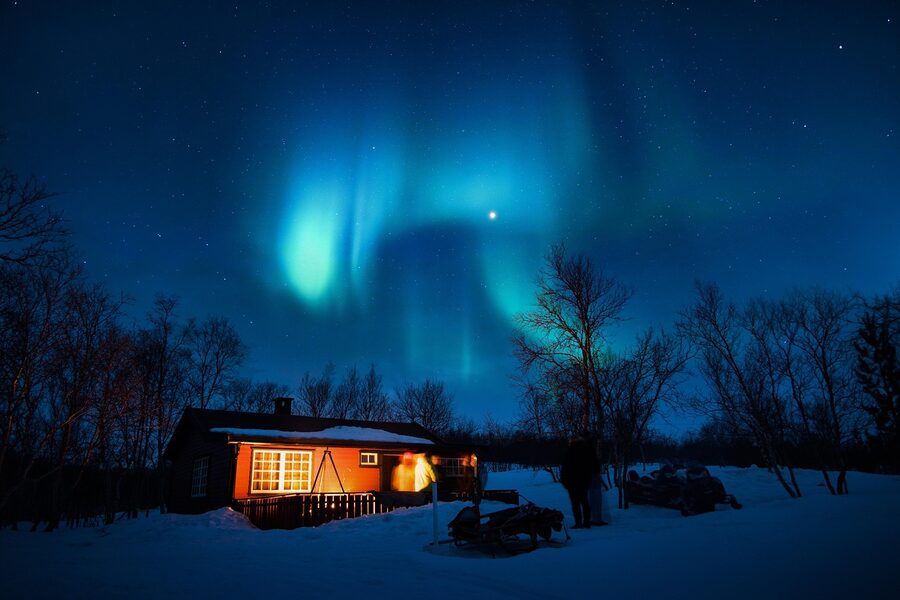 A cabin in snow under the aurora borealis on a cold night