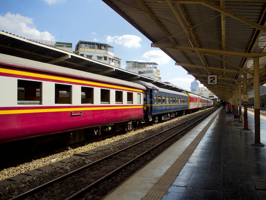 A train with colourful red and yellow carriages at an outdoor railway platform on a sunny day