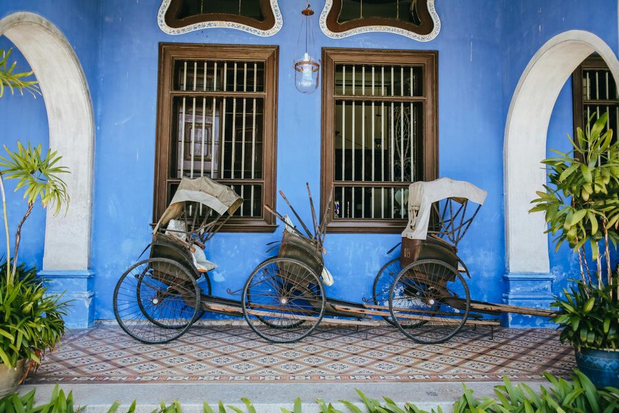 Two vintage rickshaws rest against a deep blue wall in George Town, Malaysia