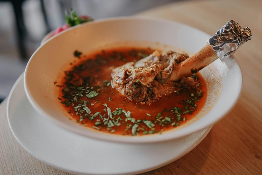 A bowl of lamb shank soup garnished with fresh herbs