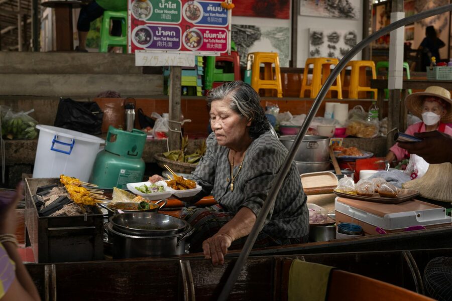 An elderly woman cooks traditional Thai dishes at a Bangkok street market