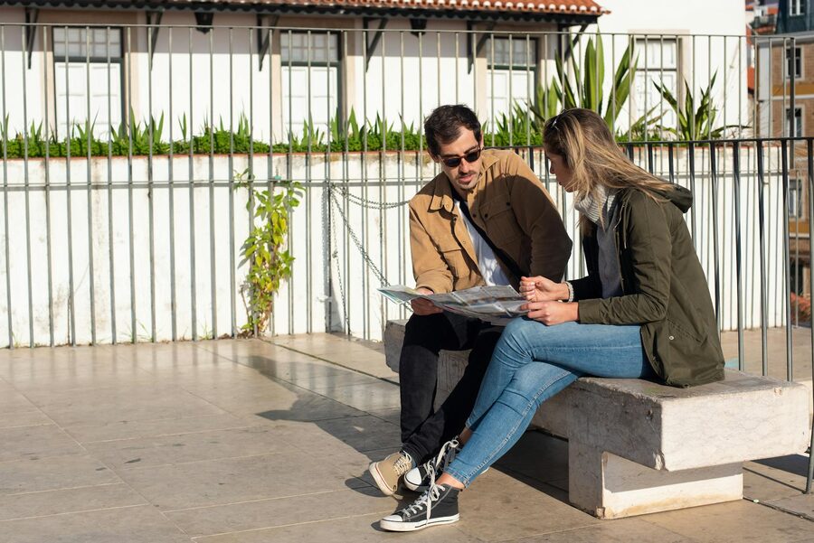A couple of tourists sitting on a bench, studying a map on a sunny day