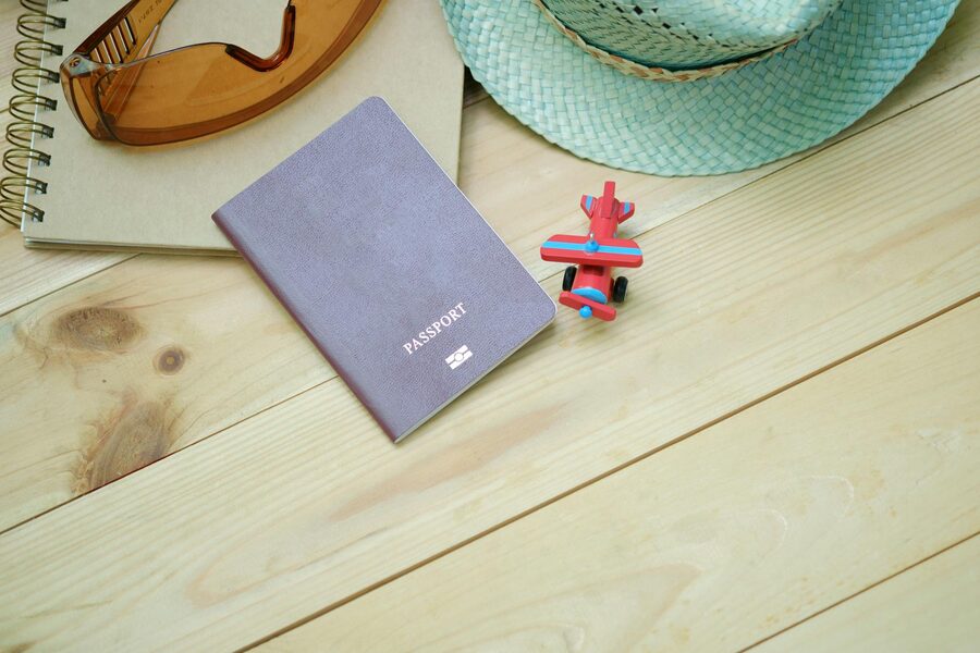 A flat lay of travel essentials including passport, notebook, toy airplane, and sunglasses